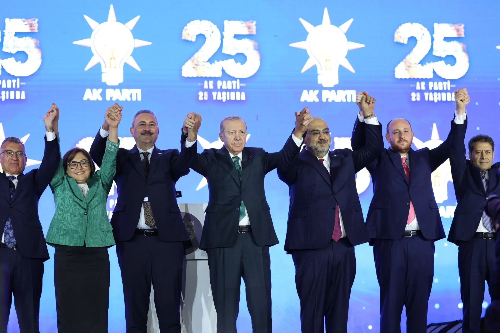 25. kuruluş yıl dönümü programında “AK Parti 25 Yaşında” görselleri önünde, partiye yeni katılanlarla birlikte sahnede el ele duran Cumhurbaşkanı Recep Tayyip Erdoğan.